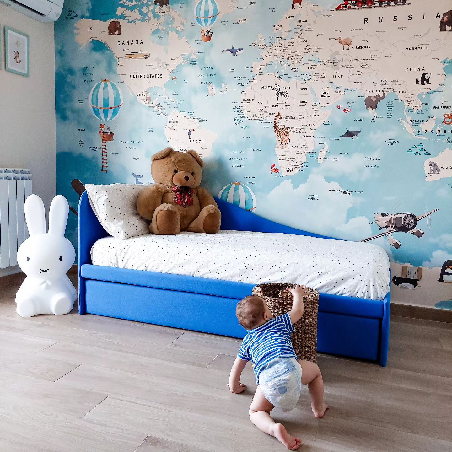 Child's bedroom with blue bed, world map wallpaper, and baby crawling.