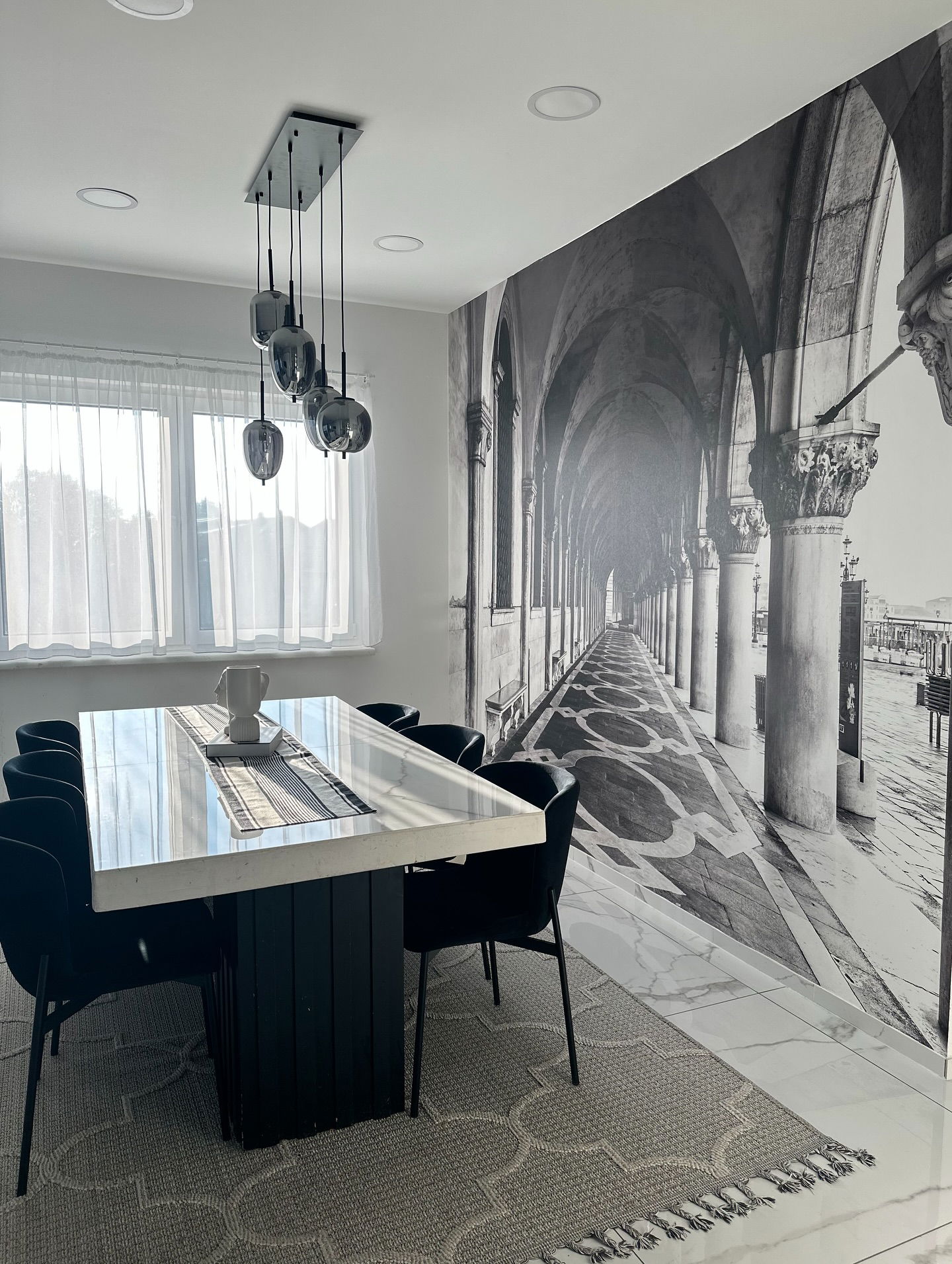 Esszimmer mit einem weißen Steintisch, schwarzen Stühlen und einem Venedig-Wandbild.