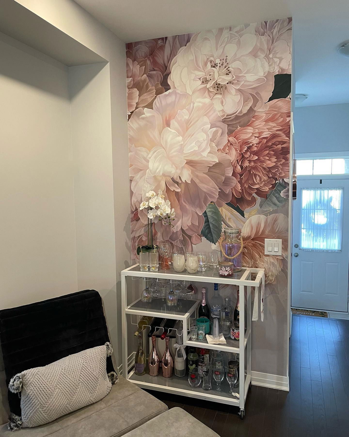 Living room with floral wallpaper, bar cart with glassware and bottles, and a gray sofa.