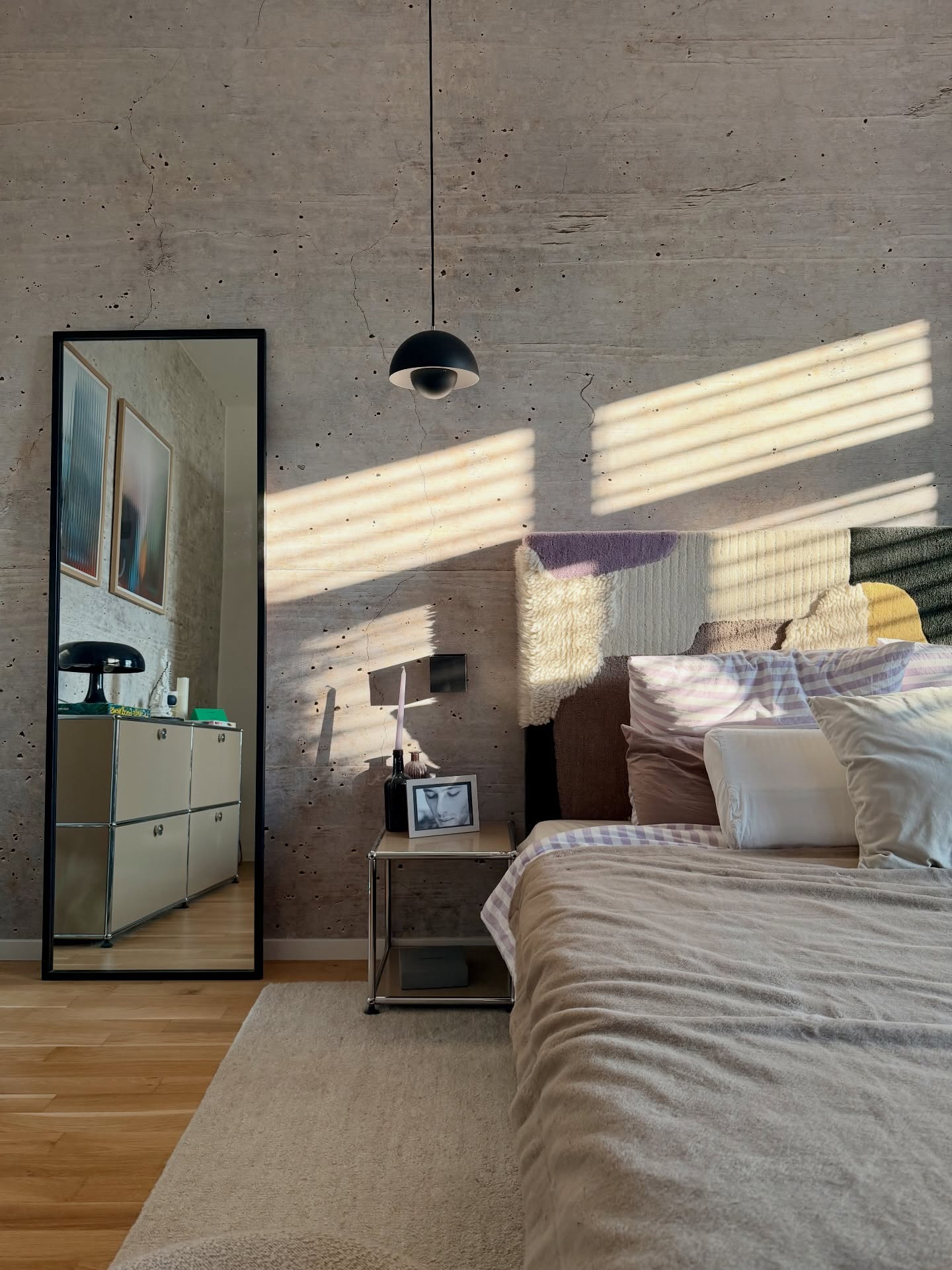 Bedroom with textured concrete wall, bed, and full-length mirror reflecting artwork.