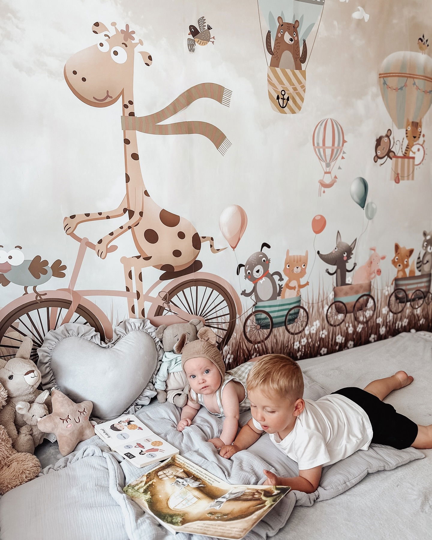 Two children reading on a bed with animal-themed wall decals.